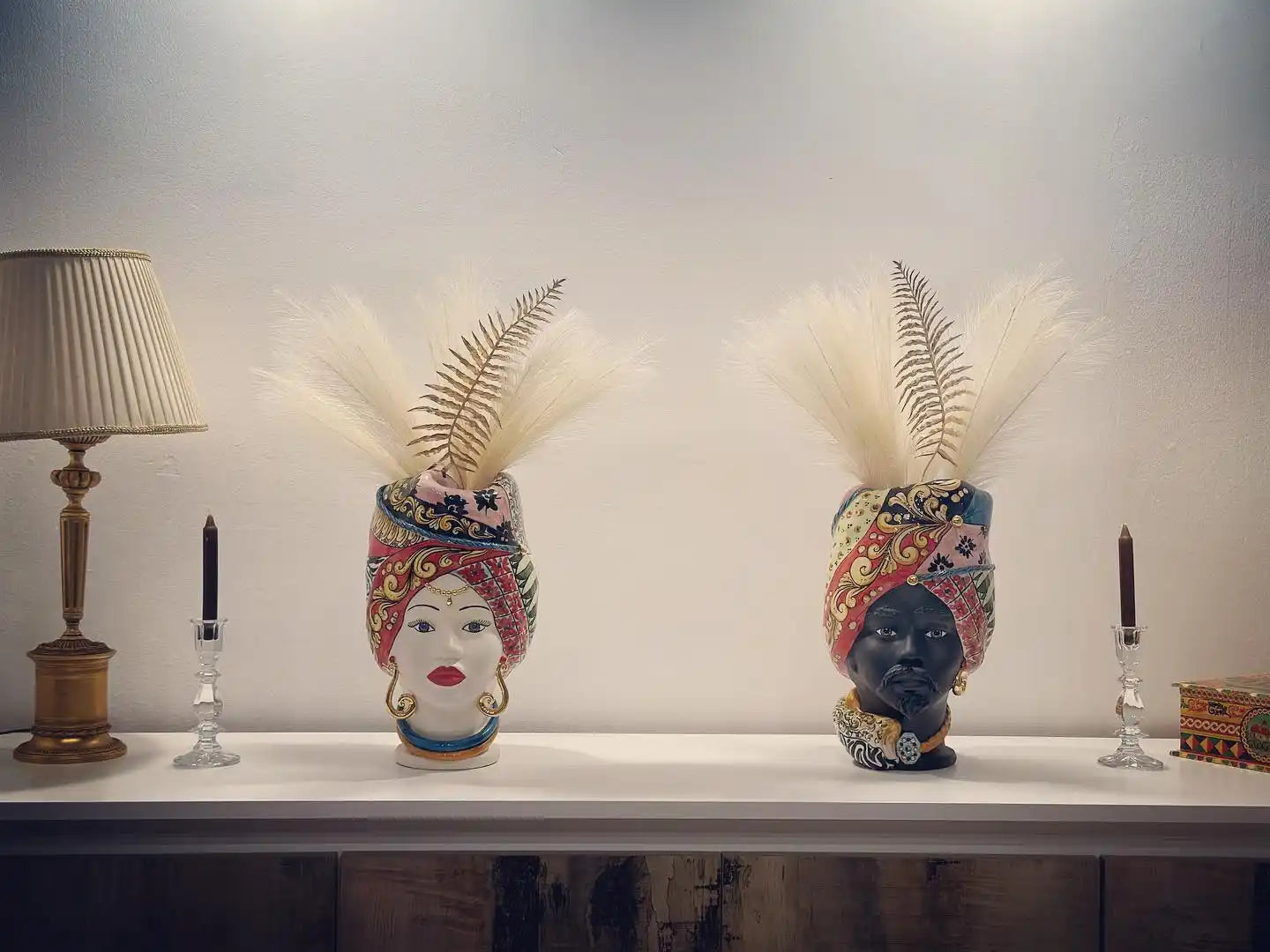 Due vasi decorativi in ceramica a forma di testa con piume e motivi colorati.