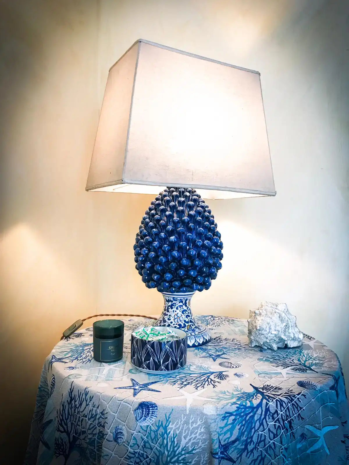 Lampada da tavolo in ceramica blu texturizzata con un paralume quadrato bianco.