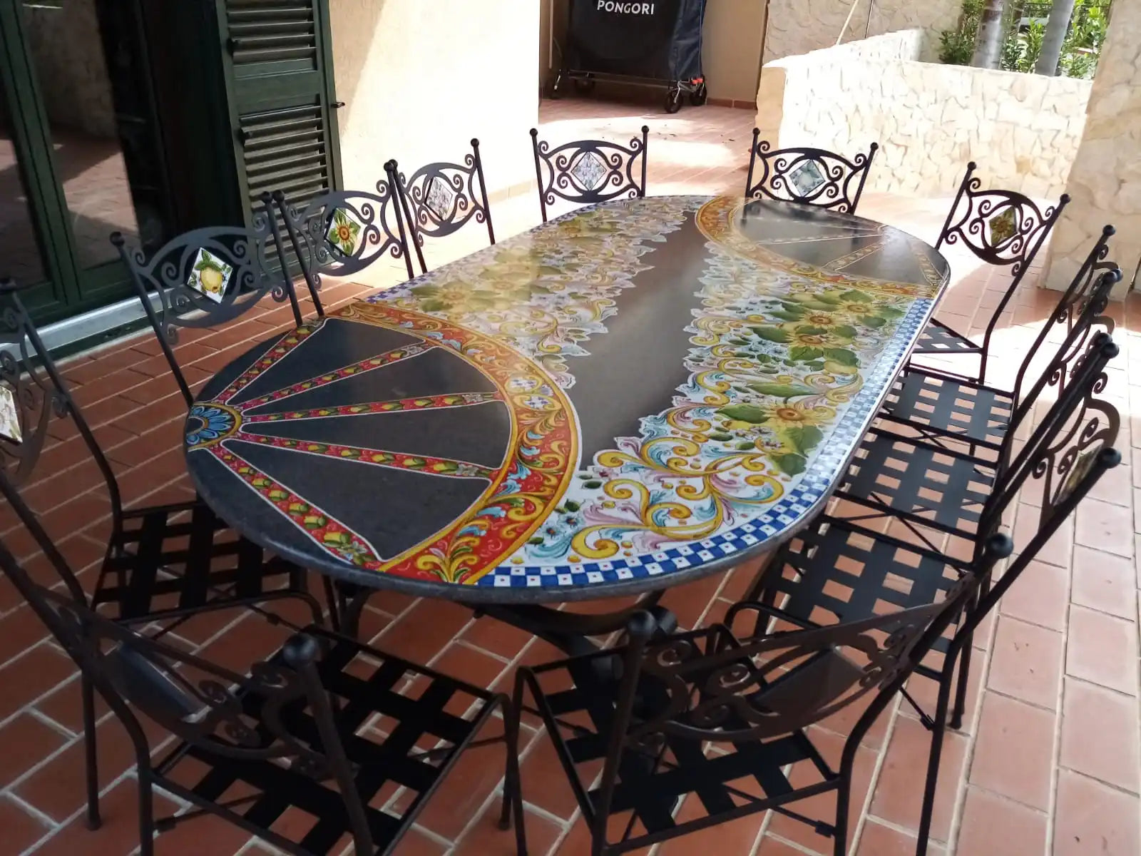 Un tavolo ovale da pranzo all'aperto con un piano in piastrelle decorativo e sedie in metallo abbinate.